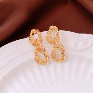 Detailed view of golden oval earrings with pleated texture on white ceramic tray