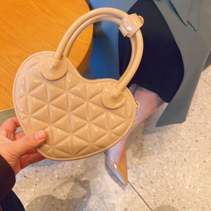 Macro shot of a beige heart-shaped bag featuring quilted patent leather with top handle