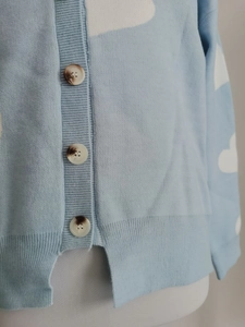 Detail of light blue knit cardigan with white cloud patterns and marble-effect buttons