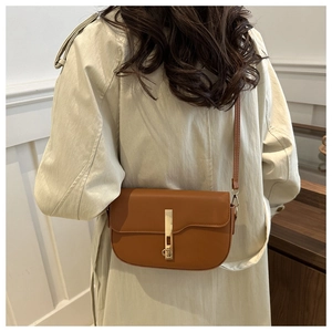 Close-up of a brown leather saddle bag with gold buckle on a model in a beige coat