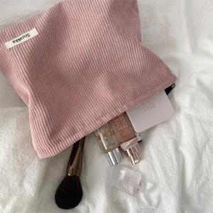 Detailed top view of pink corduroy makeup bag with cosmetics on a white textured background