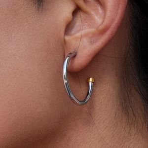 Elegant two-tone stainless steel hoop earrings with gold accents worn by a female model
