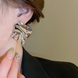 Close-up of a silver irregular crinkled metal earring worn by a model in a modern style