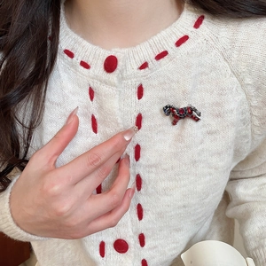 Détail de la broche cheval émaillée avec cristaux sur un cardigan en maille blanc