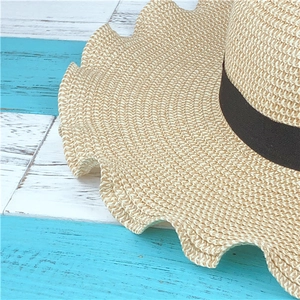 Macro detail of straw sun hat featuring a wide wavy brim and elegant black ribbon trim