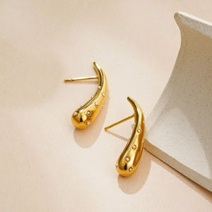 Detail showing curved 18K gold drop earrings with inlaid pearls on a minimalist background