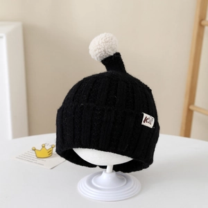 Close-up of black ribbed knit kids hat with white pom-pom and cartoon character patch