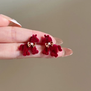 Macro shot of red flocked horse stud earrings with gold bow and pearl detail held by hand