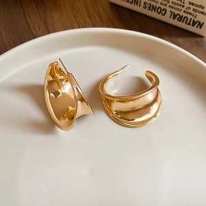 Detailed close-up of chunky gold-toned C-shaped earrings on a white display plate