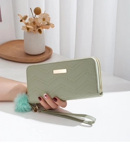 Detail view of mint green quilted wallet with gold zipper and soft plush ball pendant