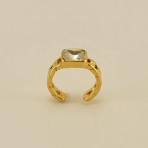 Macro shot of gold-plated open ring featuring a square clear zircon on a warm beige background