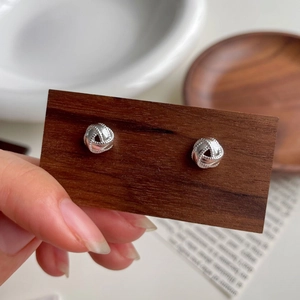 Detalle macro de pendientes de nudo en plata de ley S925 en tarjeta de madera