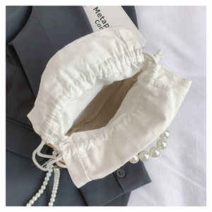 Detail view of large faux pearl handle on a cream canvas drawstring bucket bag