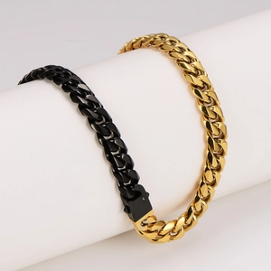 Chunky two-tone gold and black stainless steel Cuban link necklace on white pedestal