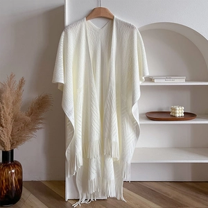 Close-up of cream white knitted shawl featuring delicate hollow patterns and tassel fringe