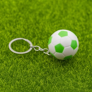 Détail macro d'un porte-clés football vert et blanc sur fond de pelouse réaliste