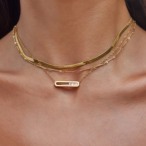 Close-up of layered gold snake chain and beaded necklace with rhinestone pendant