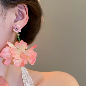 Close-up of pink fabric flower earrings with crystal tassels on a female model's ear