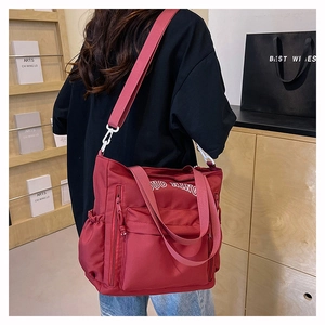 Detail of burgundy nylon tote bag showing side pockets, zippers, and sturdy shoulder strap