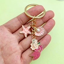Nahaufnahme goldener Schlüsselanhänger mit rosa Seestern, Muschelperle und Meerjungfrau