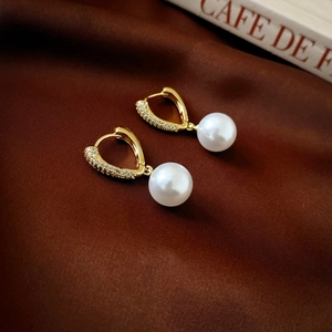Detail of luxury gold plated pearl earrings with zircon inlay on dark brown silk background