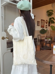 French style cream lace tote bag with floral embroidery worn by a model in a cafe
