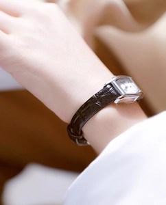 Close-up of a women's rectangular silver watch with brown croc-leather strap on wrist