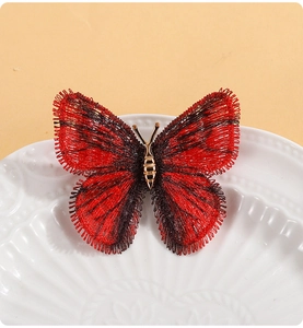 Détail d'une broche papillon brodée rouge et noir avec finitions en alliage doré