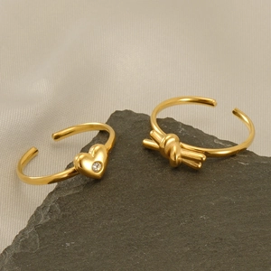 Close-up of golden heart and knot rings with diamonds on a textured stone surface