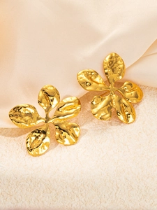 Macro detail of gold flower earrings with hammer texture finish on silk fabric background