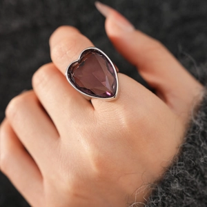 Macro shot of a heart-shaped purple zircon ring in a silver setting worn on finger