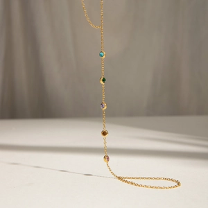 Detail of gold chain with five multi-colored round gemstones over a soft fabric background