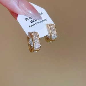 Macro detail of gold-plated rectangular hoop earrings paved with shimmering cubic zirconia