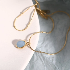 Macro shot of gold stainless steel necklace with oval blue natural stone on white stand