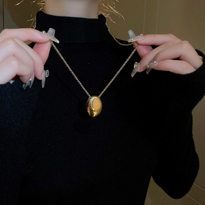 Close-up of golden oval metal pendant on black turtleneck sweater background