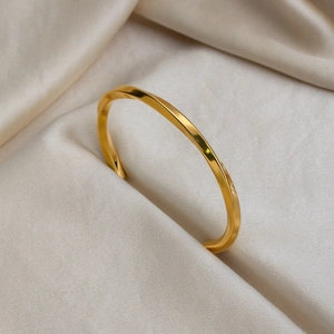 Macro view of gold twisted mobius bangle nestled in soft silk fabric folds