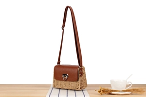 Detail of woven paper straw crossbody bag with brown leather trim on a wooden table