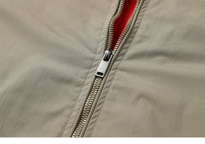 Macro view of silver metal zipper with red knit lining on beige utility jacket