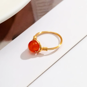 Macro view of handmade wire-wrapped gold ring featuring a bright orange gemstone bead
