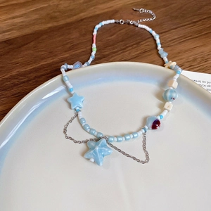 Detail of beaded shell and starfish necklace with blue stars on a white ceramic tray