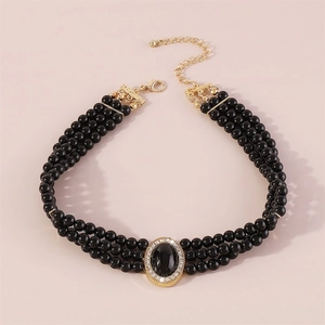 Detail of multi-layer black pearl necklace with gold cross and oval gemstone pendant