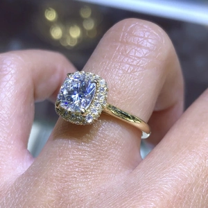 Detailed close-up of a luxurious gold halo ring with a square cut clear gemstone on a finger