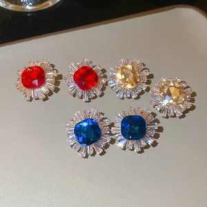 Macro view of sunburst stud earrings with red, blue, and yellow crystals on leather