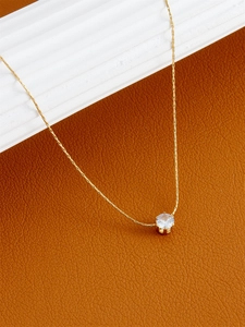 Macro detail of a minimalist gold necklace with a brilliant round-cut zircon pendant