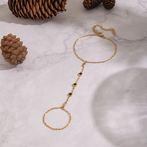 Golden stainless steel hand chain ring with green zircon stones on marble background