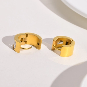 Detail of gold huggie hoop earrings with brushed metal finish and single zircon stone