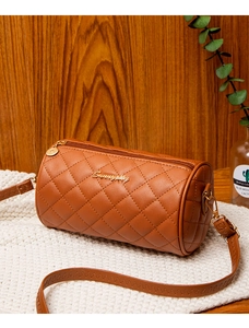 Brown quilted cylinder crossbody bag with gold zipper detail on white knit fabric