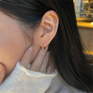 Close-up of minimalist golden hexagonal earrings worn on ear with soft lighting