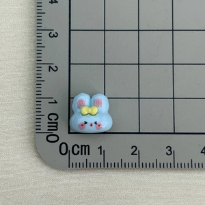 Detailed size view of a small blue resin rabbit charm on a centimeter grid mat