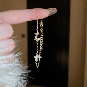 Detail of gold-plated butterfly bracelet with zircon and white shell charms on wrist
